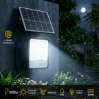 Solar light fixture with solar panel on a wall at night, surrounded by plants.