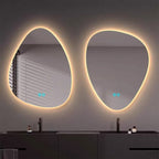 Two organic-shaped LED backlit mirrors mounted on a dark gray wall above a double vanity with black faucets and small bottles.